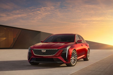 A red Cadillac CT4 with a dark grille and silver wheels, parked on a paved surface at sunset.