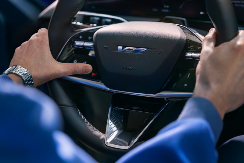 Close-up of a Man About to Press the V-Button on the 2026 OPTIQ-V Steering Wheel | Cadillac of Memphis in Memphis TN